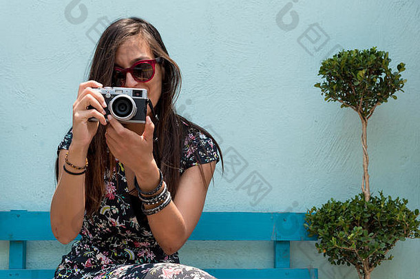 墨西哥乔鲁拉，一名戴着太阳镜的妇女<strong>手持</strong>复古相机在户外<strong>拍照</strong>