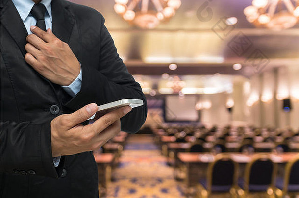 商人在会议厅或研讨会室背景的抽象模糊照片上使用智能手机