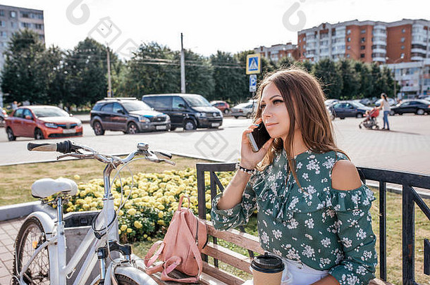 美丽的女孩坐着板凳上自行车袋夏天新鲜的空气生活方式城<strong>市调</strong>用电话手杯咖啡概念