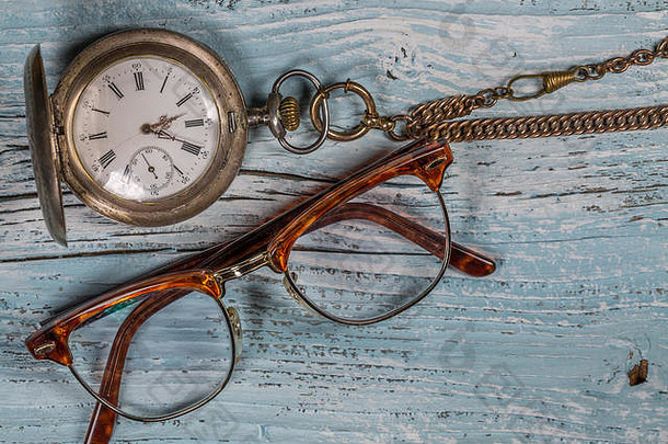 木制桌子上的古董银怀表和眼镜