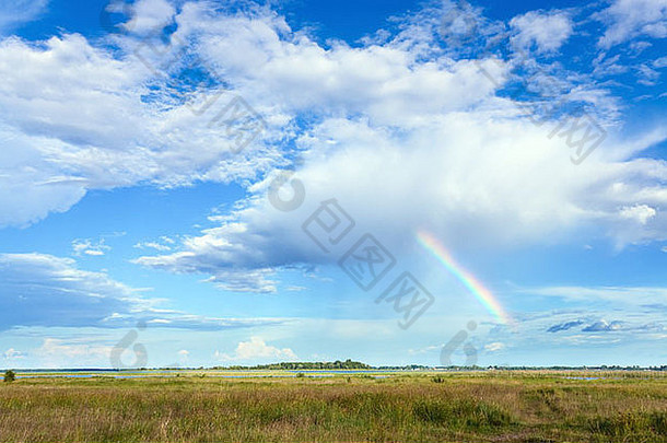 <strong>彩虹</strong>在蓝色多云的天空中，在夏天的草地上。