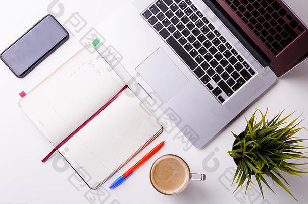 白色桌子上笔记本平板电脑空白笔记本绿色花电话杯咖啡
