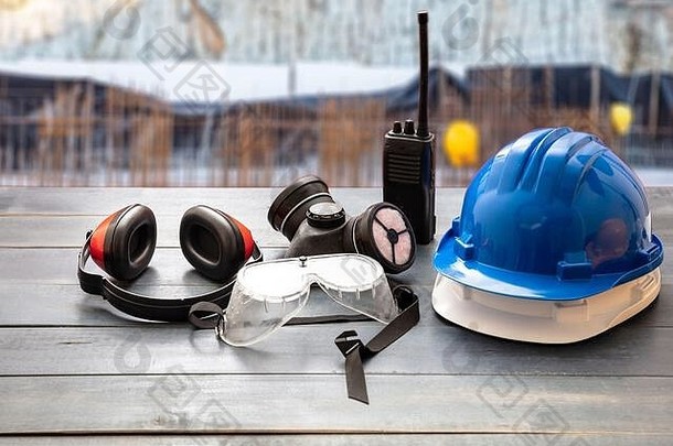 <strong>安全生产</strong>防护设备。木制工作台上的工业防护装备，模糊了施工现场背景。安全帽、耳罩、呼吸面罩、，
