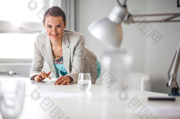 一幅年轻快乐的女商人倚在办公桌上使用数字平板电脑的照片