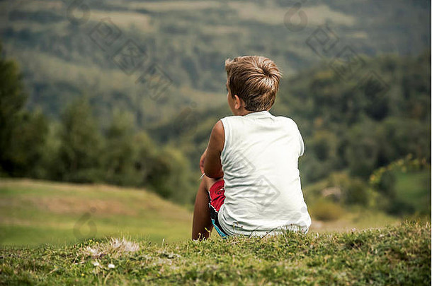 男孩坐在山上，望着远处。童年、梦想、自由——一个概念。
