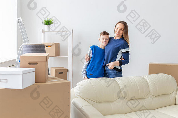 笑容满面的单身母亲和迷人的儿子正站在一间明亮舒适的新公寓里摆姿势。新房的搬家和抵押的概念
