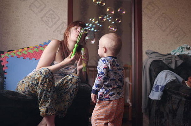年轻的美丽的女人吹肥皂泡沫婴儿男孩戏剧捕捉幸福的微笑内部房间慢运动视频