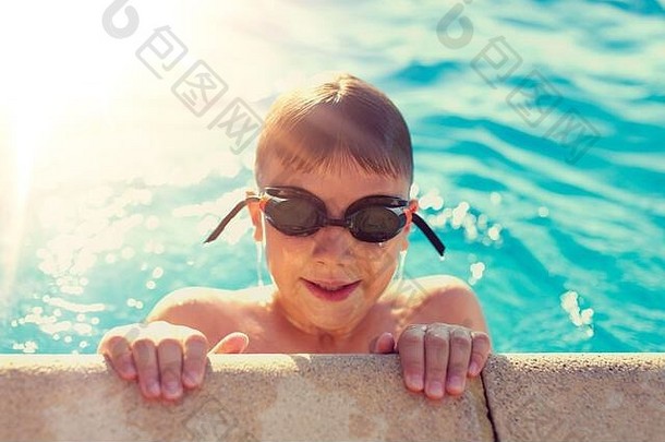 在阳光明媚的<strong>夏日</strong>里，戴着护目镜的快乐的小男孩抱着<strong>游泳</strong>池的边缘