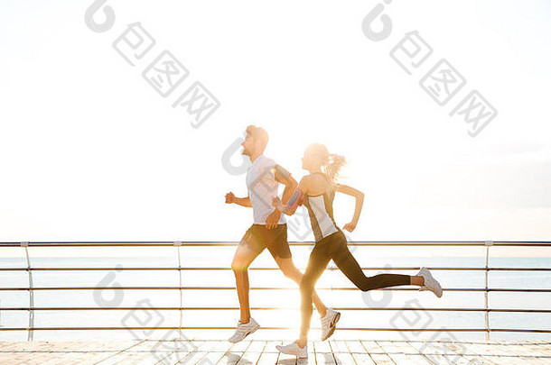 日落时分，一对年轻的运动型情侣在木制码头上奔跑