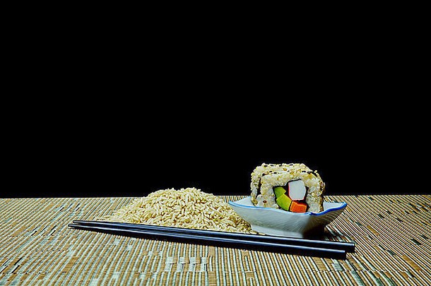 生的和熟的天然有机糙米鳄梨素食寿司，筷子在黑色背景上隔离