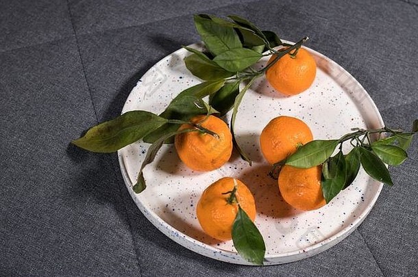 白色陶瓷盘上的绿叶橘子和灰色厨房毛巾