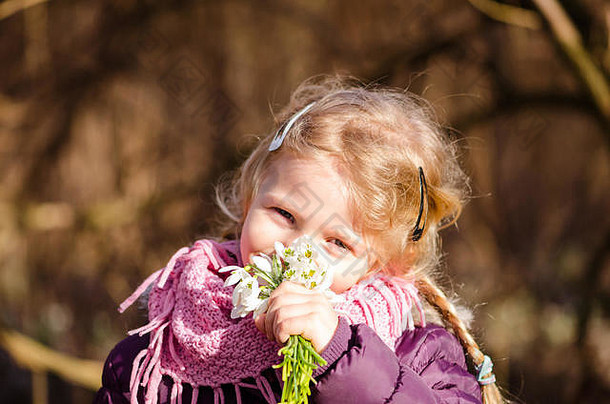 在阳光明媚的日子里，一个美丽可爱的女孩在手上嗅着白色的雪花莲