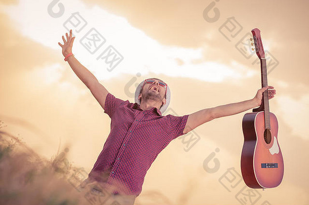 麦田上手持原声吉他的欢快音乐演奏者。背景中的太阳和云。自由、音乐、艺术和生活方式理念。