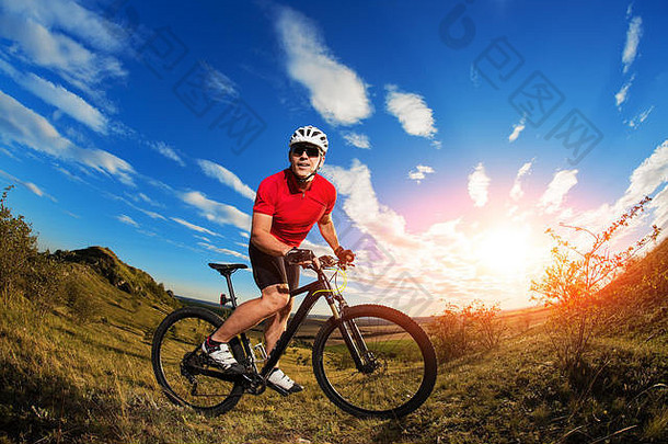 骑山地自行车的旅游者。秋天的风景。穿着红色运动衫和白色头盔骑自行车的运动员