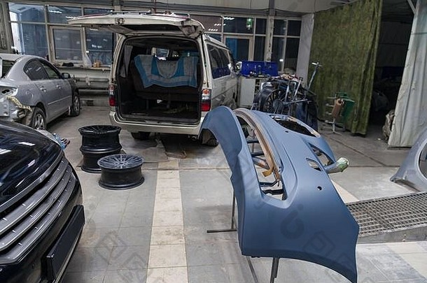 汽车保险杠零件在房间内的汽车修理车间喷漆后在机架上，并配有维修车身零件的工具和设备