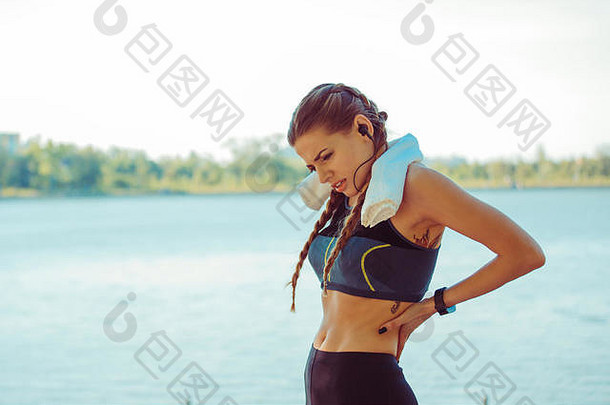 背痛。身穿<strong>蓝黑色</strong>运动服的女运动员站在海边，摩擦着她的下背部肌肉，半身躯干肖像。