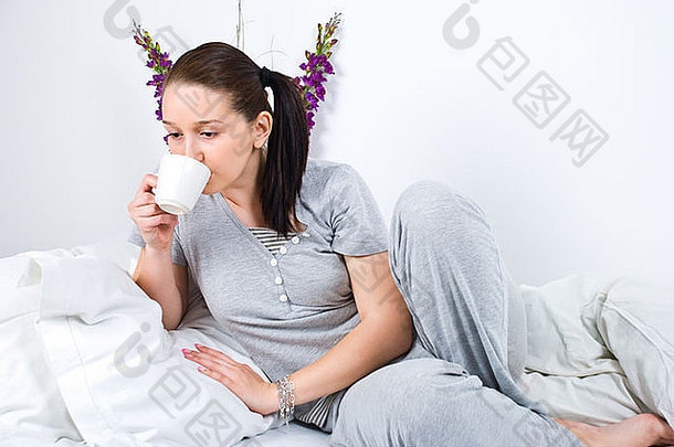 年轻女子喝着一杯咖啡，早上躺在床上