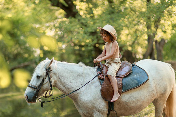一个卷发的小男孩，穿着哈比人的衣服，在夏日森林里和马玩耍。