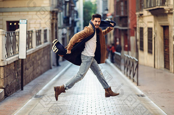 年轻快乐的男人穿着冬衣在城市背景下跳跃