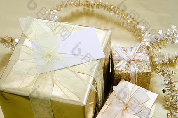 一组用<strong>金箔纸</strong>包裹的圣诞礼物，金色反光面上有丝带，背景是金属丝花环。