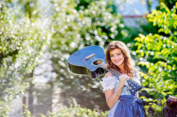 穿着传统巴伐利亚服装手持吉他的美丽年轻女子