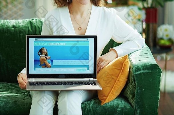 在阳光明媚的日子里，一位身穿白色上衣的女士在家里展示带医疗保险网站的笔记本电脑的特写镜头。