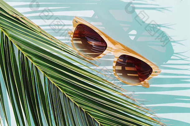 在棕榈叶和绿松石背景上俯视米色太阳镜，无人。旅游概念对象