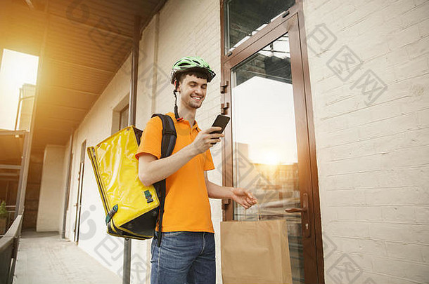 一个穿着黄衬衫的年轻人用小玩意跟踪城市街道上的订单，运送比萨饼。使用在线应用程序接收和跟踪发货地址的快递员。现代技术。