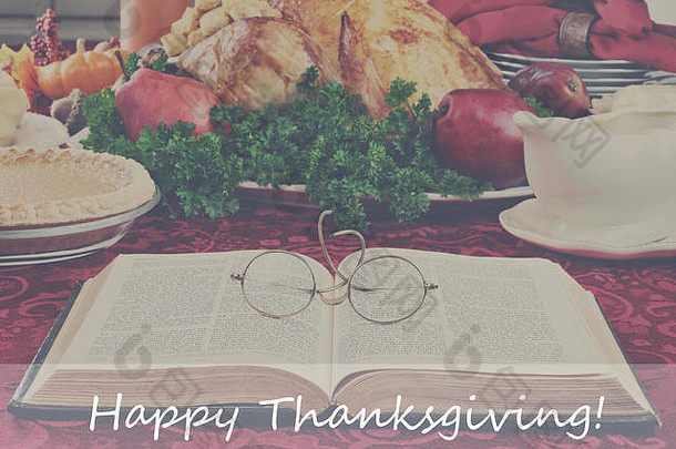 过滤后的图像是一本打开的圣经，杯子放在节日餐桌上，背景是准备好的火鸡和装饰物，感恩节快乐