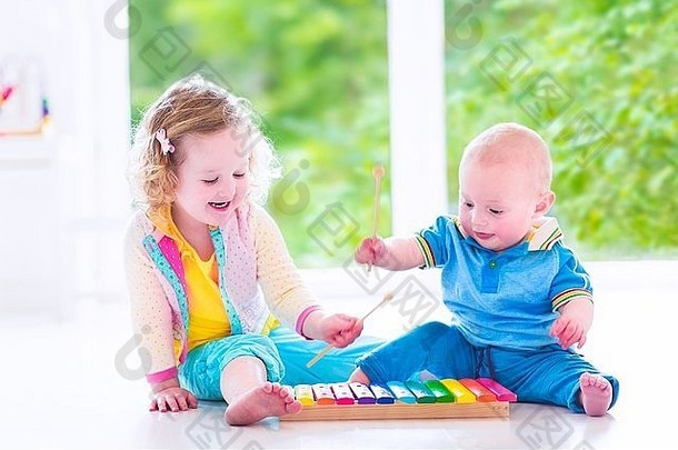 两个小孩——可爱的卷发蹒跚学步的小女孩和一个有趣的小男孩，兄弟姐妹在演奏音乐，玩木琴