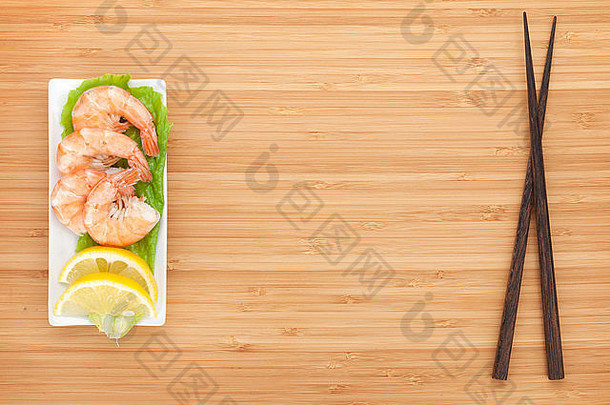 用柠檬和筷子煮的虾。带复印空间的木桌上的俯视图