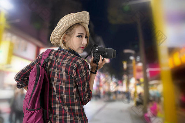 在中国夜市五颜六色的霓虹灯下行走的旅游女孩手里拿着相机。