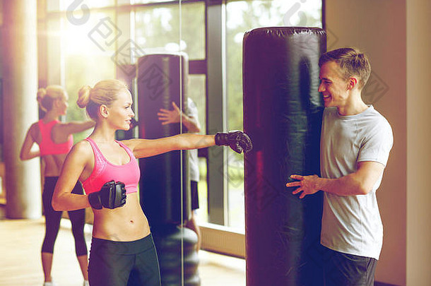 微笑的女人与私人教练在健身房拳击