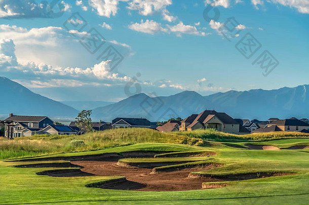 阳光明媚的日子里，以房屋和山脉为背景的高尔夫球场