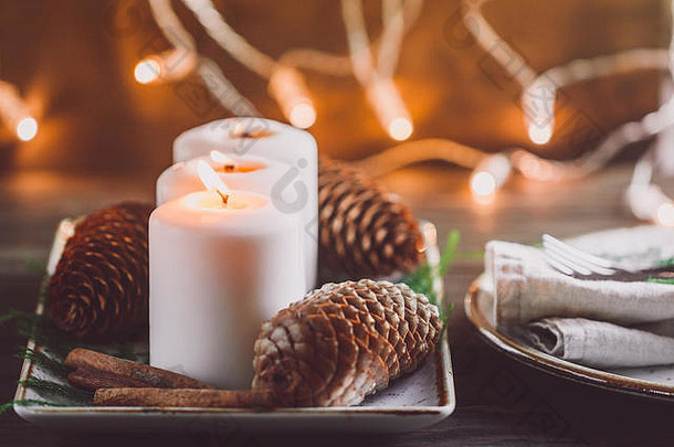 冬季舒适的装饰，木制节日桌上有白色燃烧的蜡烛，背景上有模糊的灯光。