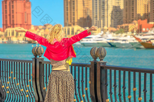 卡塔尔的旅游业。在码头走道上，一位金发碧眼的优雅女士注视着卡塔尔珍珠港——<strong>阿拉伯</strong>港。无忧无虑的游客在多哈张开双臂