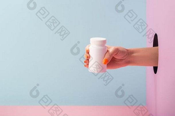 女人的手拿着一瓶蓝色和粉色背景的白色药丸