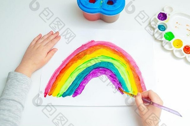 俯视图孩子正在纸上用水彩画彩虹。创意概念。