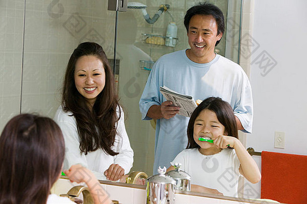 家庭在浴室里为一天做准备的镜子反射，女儿刷牙