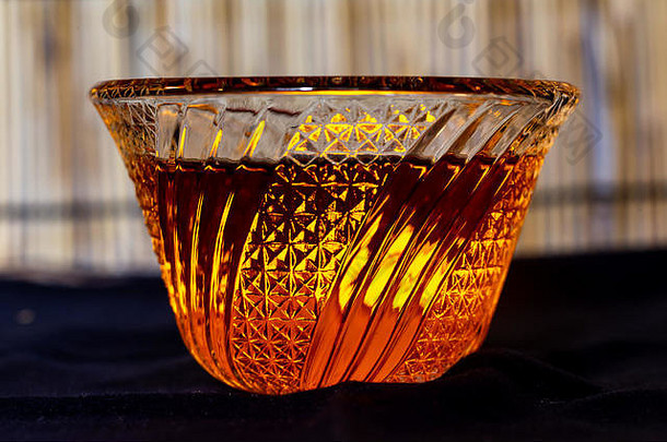 在一个装饰精美的切割玻璃碗里的有色液体，由一根小电蜡烛照亮。