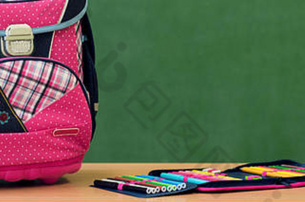 靠着绿板的书桌上放着粉红色的少女装书包和铅笔盒。开学第一天的概念。