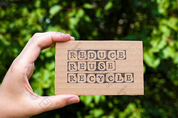 女人手持有纸板卡单词减少重用回收使黑色的字母邮票相反绿色花背景