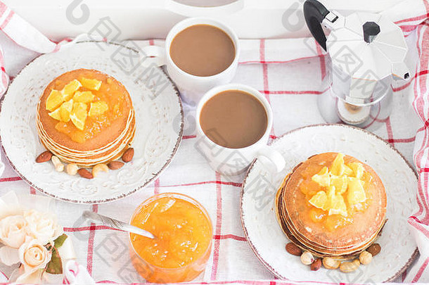 托盘上两人的浪漫传统早餐。美式煎饼，陈年盘子上有橘子酱和坚果，还有两个白咖啡杯和意大利甜点
