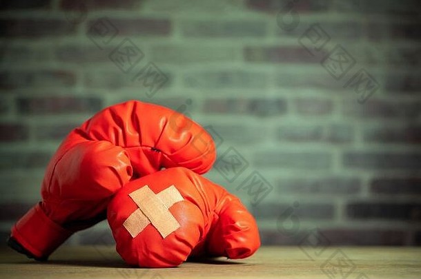 红色拳击手套放在运动体育馆的木桌和砖墙上。拳击手套上的胶布相互交叉。受伤或战斗的想法
