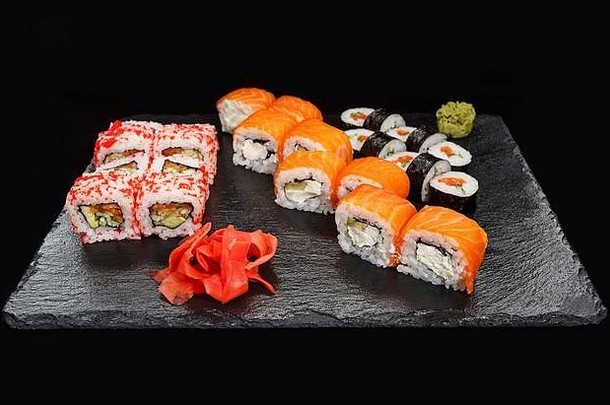 不同类型的日本寿司，传统的卷饼和黑石板上有芥末和生姜的maki。