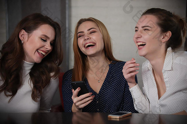 三个年轻漂亮的女人坐在酒吧里看着电话，笑着