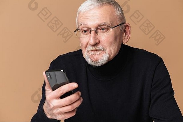 一位头发灰白、胡子灰白、戴眼镜、穿着毛衣的迷人老人，在米色背景下，惊奇地看着手机