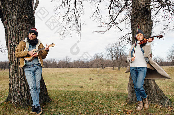 两个穿着暖和的音乐家站在树下演奏的场景