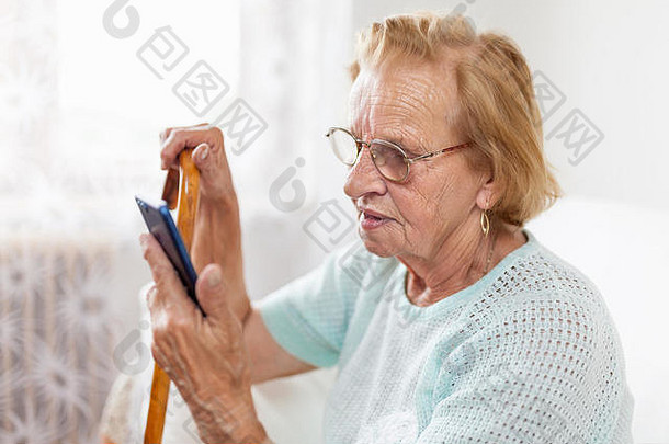 戴眼镜和手杖使用手机的老年妇女