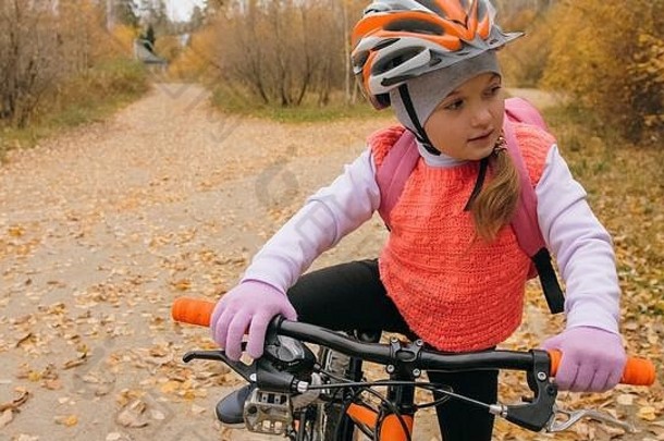一个白人孩子在秋天公园里骑自行车散步。小女孩在森林里骑着黑橙色的自行车。这孩子去做自行车运动。骑自行车的运动骑乘